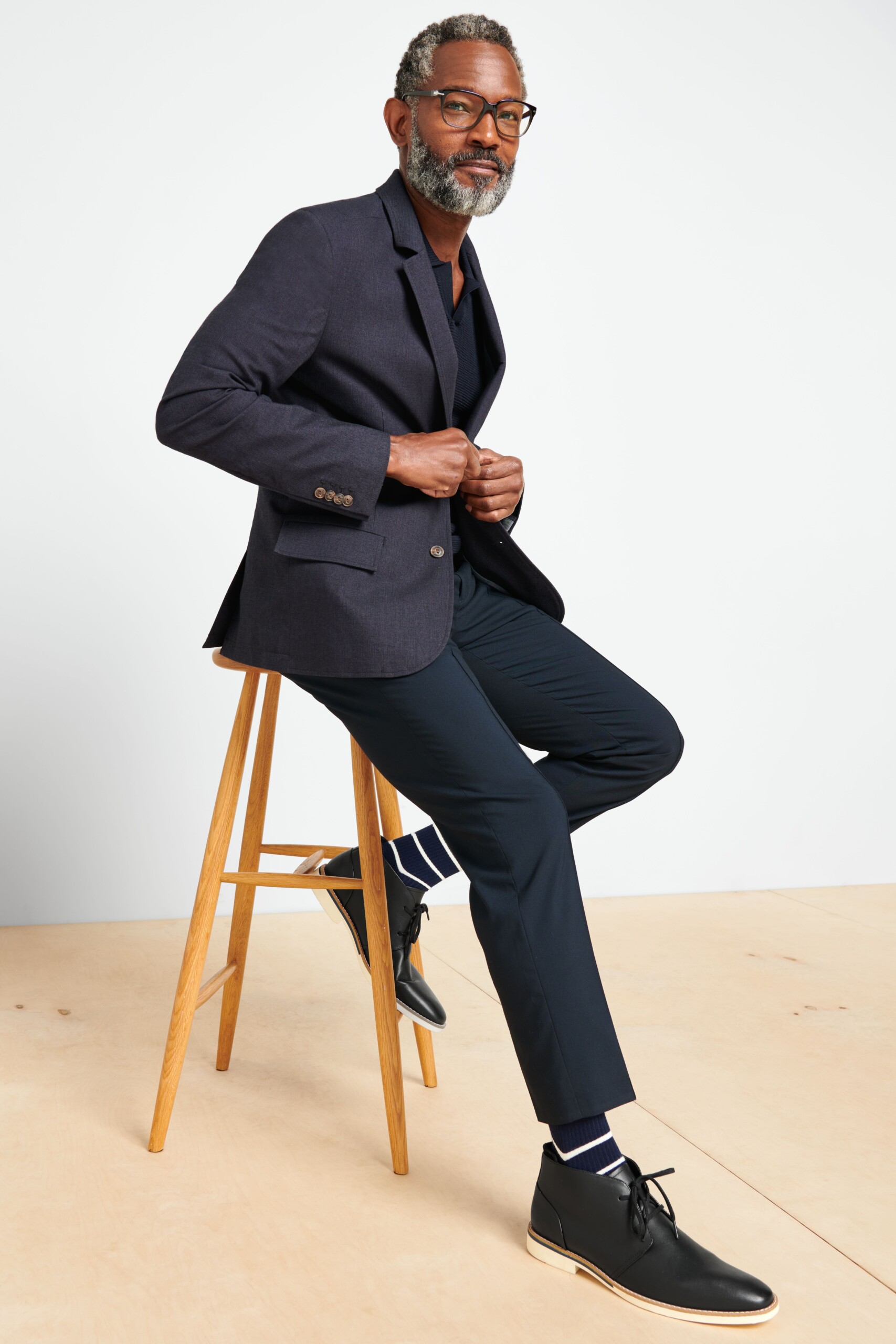 Stitch Fix model wearing men’s graduation outfit featuring a navy suit jacket, navy pants, striped socks and black dress shoes.