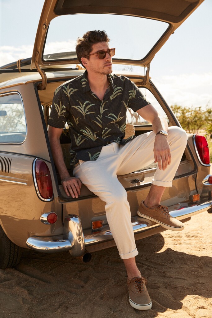 Stitch Fix model wearing men’s 4th of July outfit with navy and green palm print shirt, tan pants, tan shoes sitting in car.