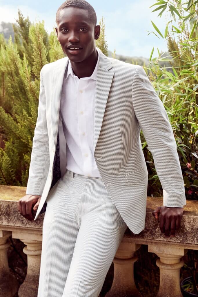 Stitch Fix model wearing men’s cocktail wedding attire outfit with blue seersucker pants, matching blazer, white dress shirt.