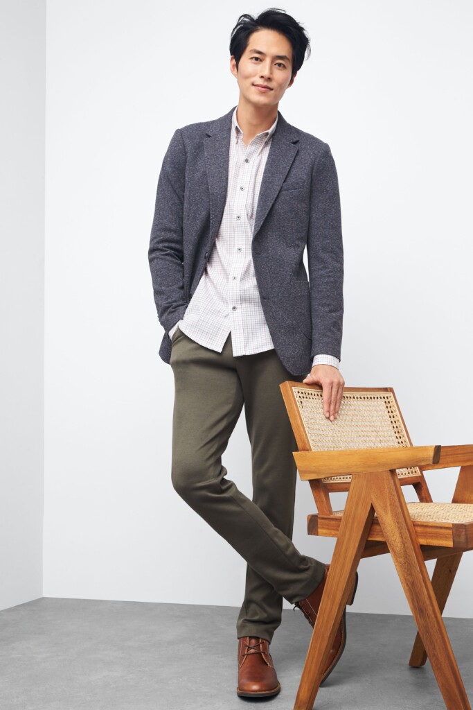 Stitch Fix model wearing men’s casual wedding attire outfit with dark green chinos, button-up shirt, navy blazer, tan shoes.