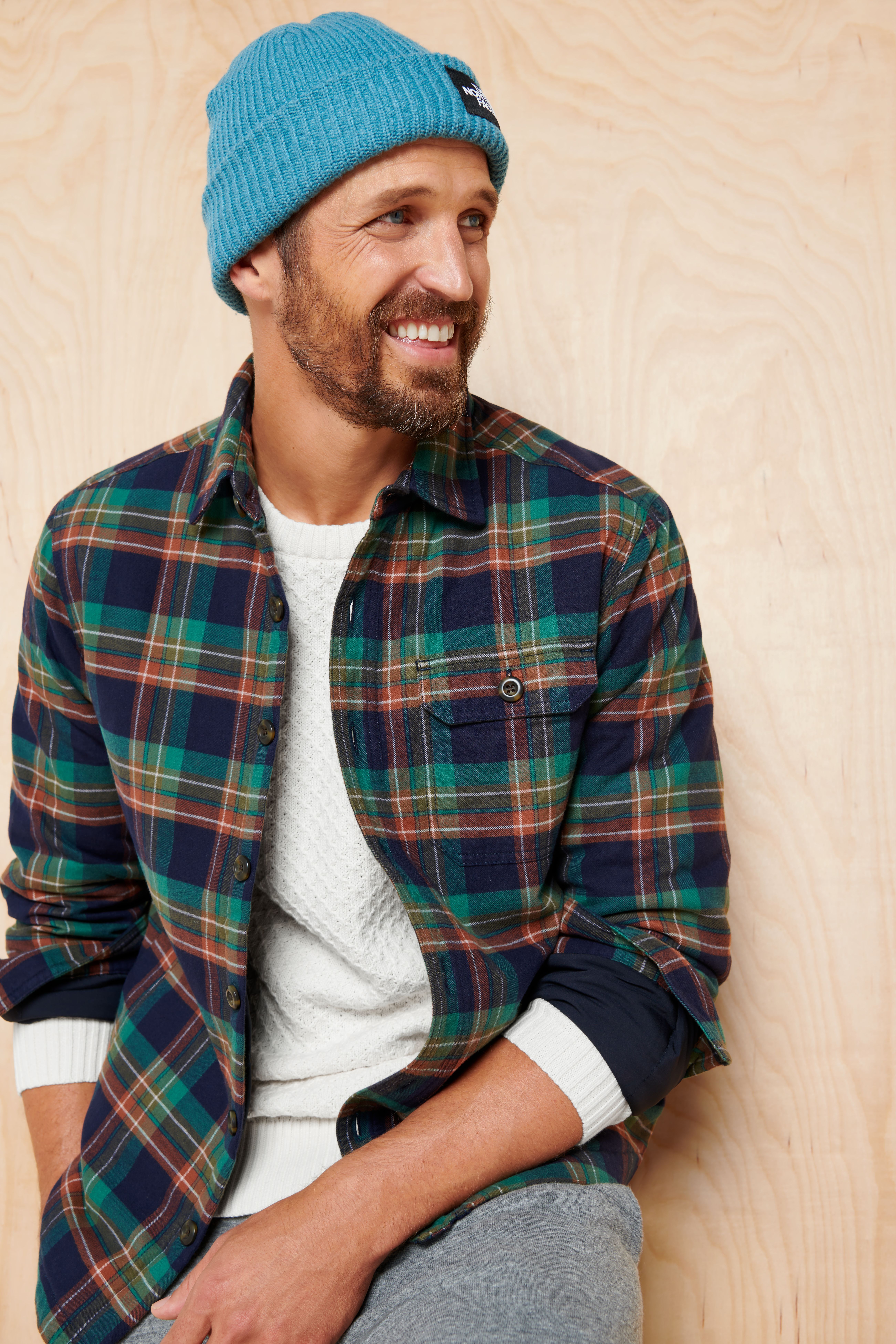 Stitch Fix model wearing Y2K fashion for men outfit with white tee, flannel shacket, grey joggers, blue beanie.