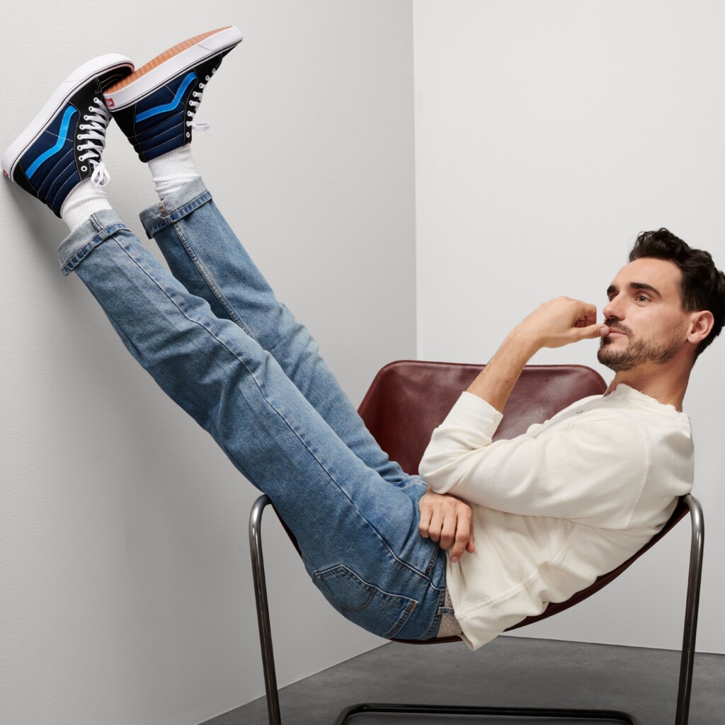 Stitch Fix model wearing Y2K fashion for men outfit with white long-sleeved tee, blue jeans, navy high-top sneakers.