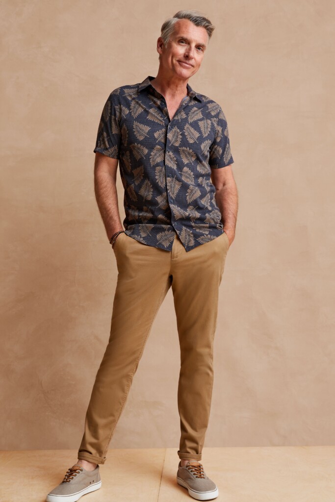 Stitch Fix model wearing men’s wedding attire outfit with brown chinos, navy palm print short-sleeved shirt and tan sneakers.