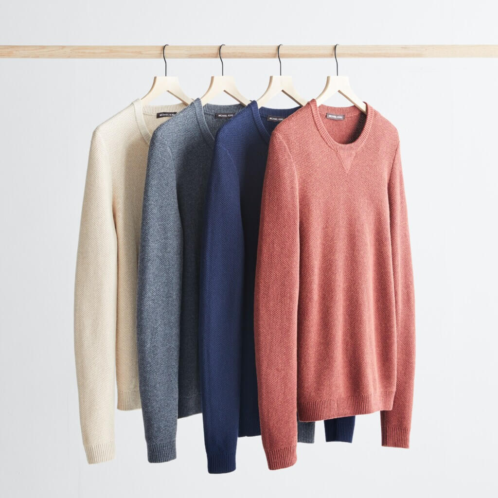 Stitch Fix men's business casual sweaters in beige, grey, navy and coral hanging on a rack.