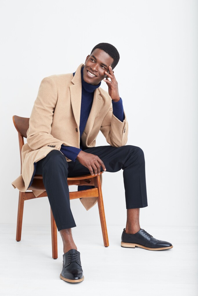 Stitch Fix model wearing black men’s fall shoes, black trousers, blue turtleneck and tan blazer.