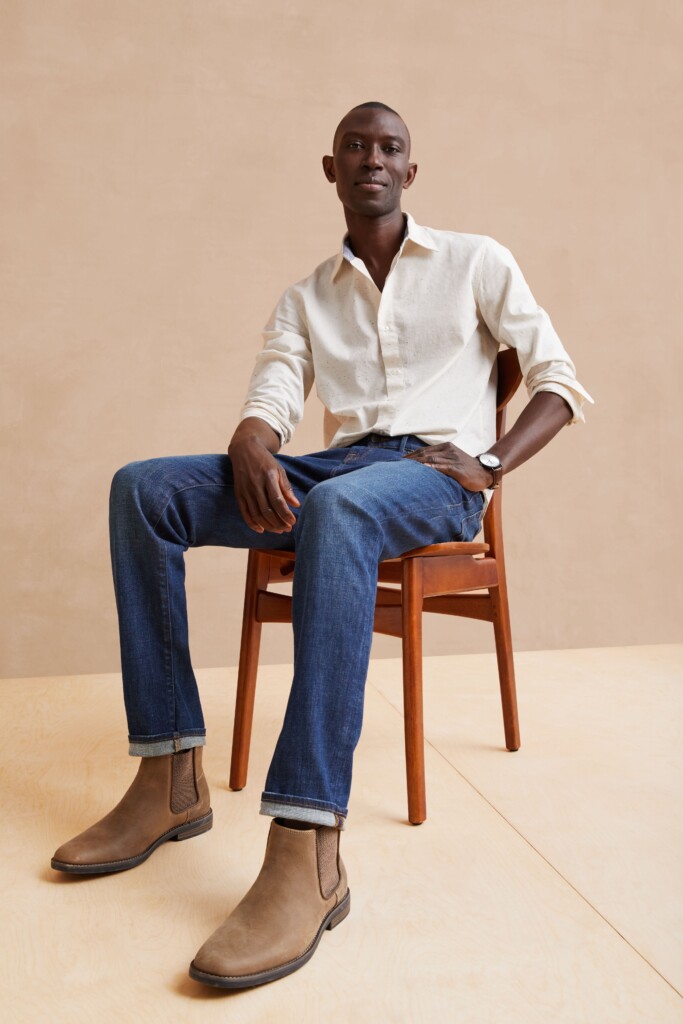 Stitch Fix model wearing men’s fall shoes outfit with Chelsea boots, blue jeans and a cream long-sleeve button-down shirt.