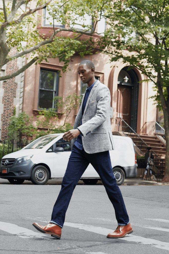 Stitch Fix model wearing men’s fall shoes outfit with brown dress shoes, dark-wash denim, blue sweater and grey blazer.
