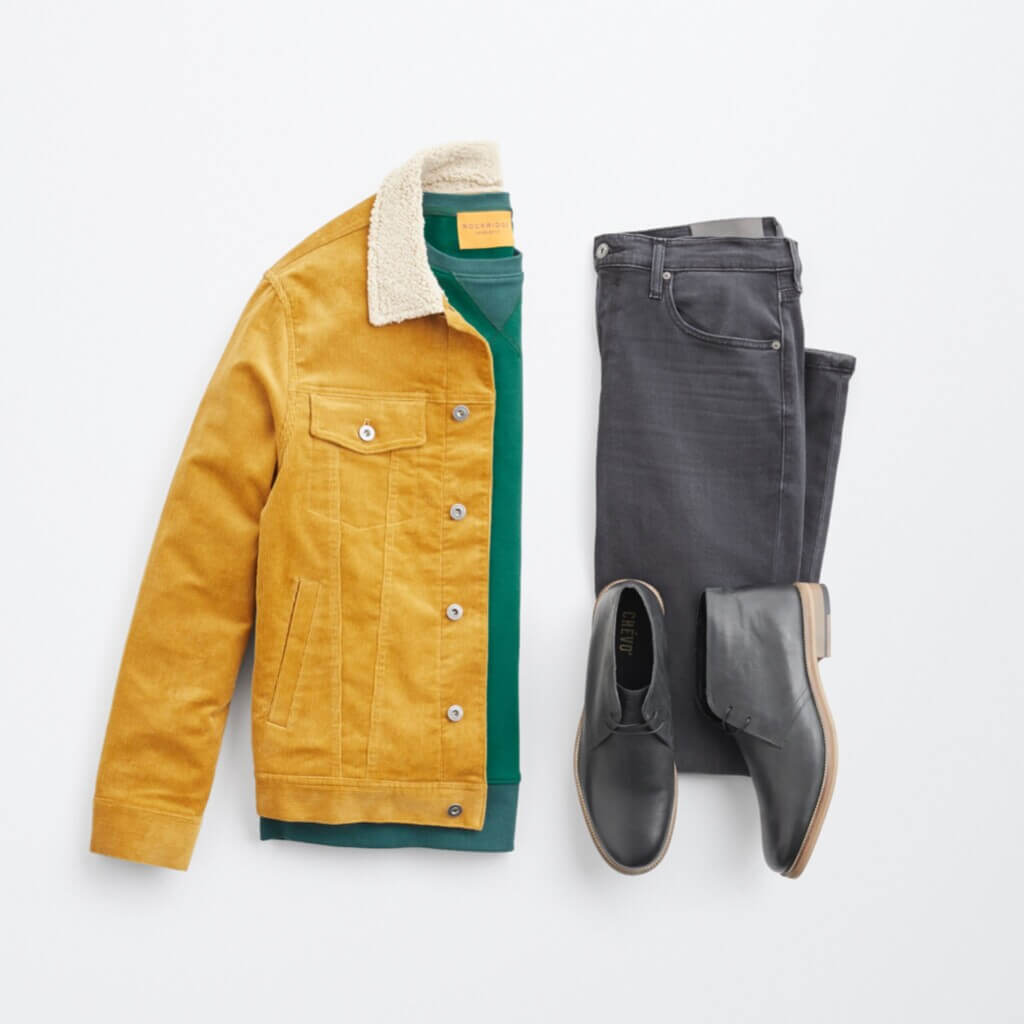 Stitch Fix Men’s cabincore outfit laydown with green pullover, mustard corduroy jacket, grey jeans and grey boots.