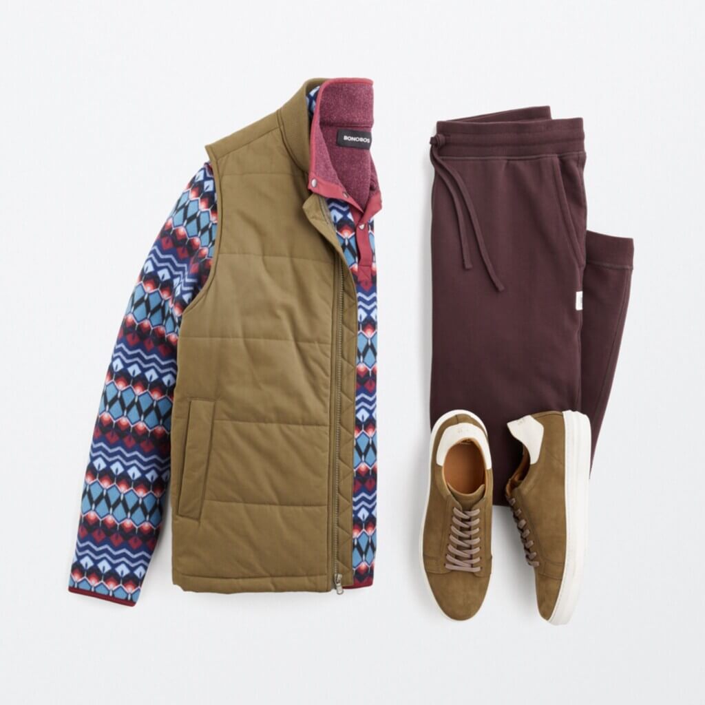 Stitch Fix Men’s cabincore outfit laydown with Southwestern print pullover, olive vest, burgundy joggers and brown sneakers.