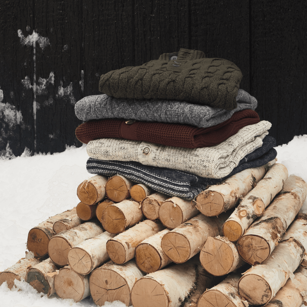Stitch Fix Men’s stack of cardigans in various colors on top of a pile of firewood.
