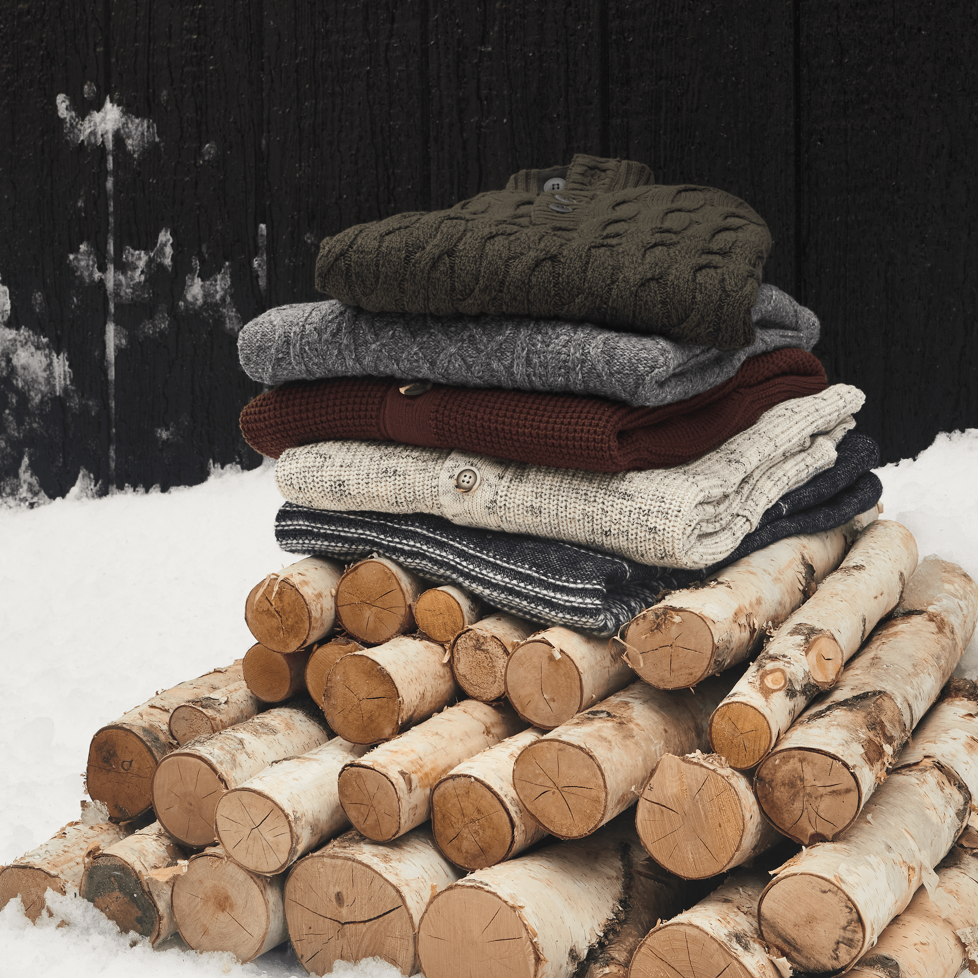 Stitch Fix Men’s stack of cardigans in various colors on top of a pile of firewood.