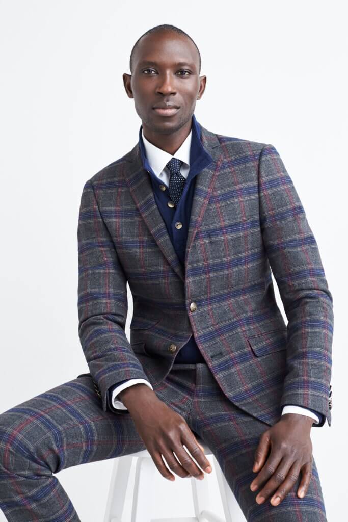 Stitch Fix model wearing men’s fall wedding attire with plaid blazer, matching dress pants, navy sweater, white shirt, tie.