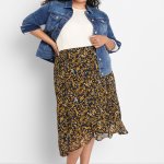 Stitch Fix model wearing plus-size clothing featuring white knit top, denim jacket, floral print skirt and black flats.