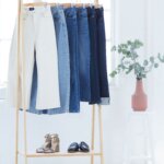 Stitch Fix Women’s rack with white, light blue, classic blue, and dark blue jeans hanging with shoes under, next to a plant.