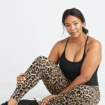 Stitch Fix model sitting in plus-size clothing featuring black cami, leopard print leggings and black and white sneakers.