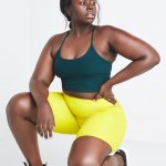 Stitch Fix model kneeling in plus-size clothing featuring green thin strap crop tank, yellow biker shorts and black sneakers