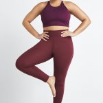 Stitch Fix model in yoga pose wearing plus-size clothing featuring purple sports bra and burgundy leggings.