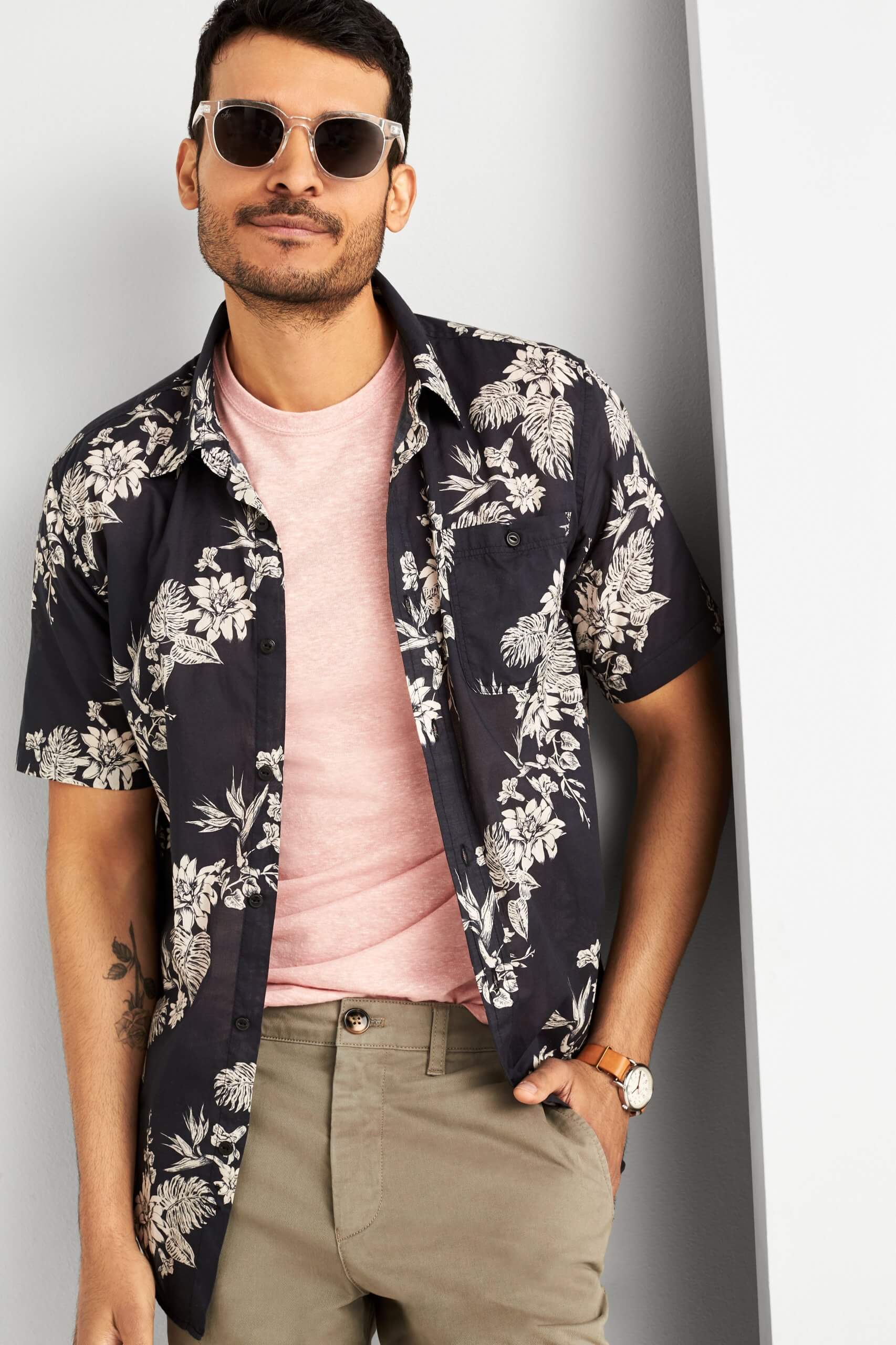 Stitch Fix model wearing a pink T-shirt, navy floral button-up shirt and tan shorts with sunglasses and brown leather watch.