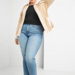 Stitch Fix model wearing plus-size clothing featuring black knit top, tan jacket, light wash jeans and animal print booties.