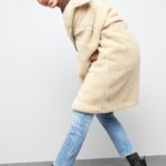 Stitch Fix women’s model in boots with jeans outfit with black combat boots, light-wash jeans, mauve sweater and teddy-bear coat.