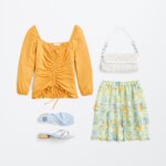 Stitch Fix women’s regencycore outfit featuring floral mini skirt, yellow ruched long-sleeve top, white purse and blue sandals.