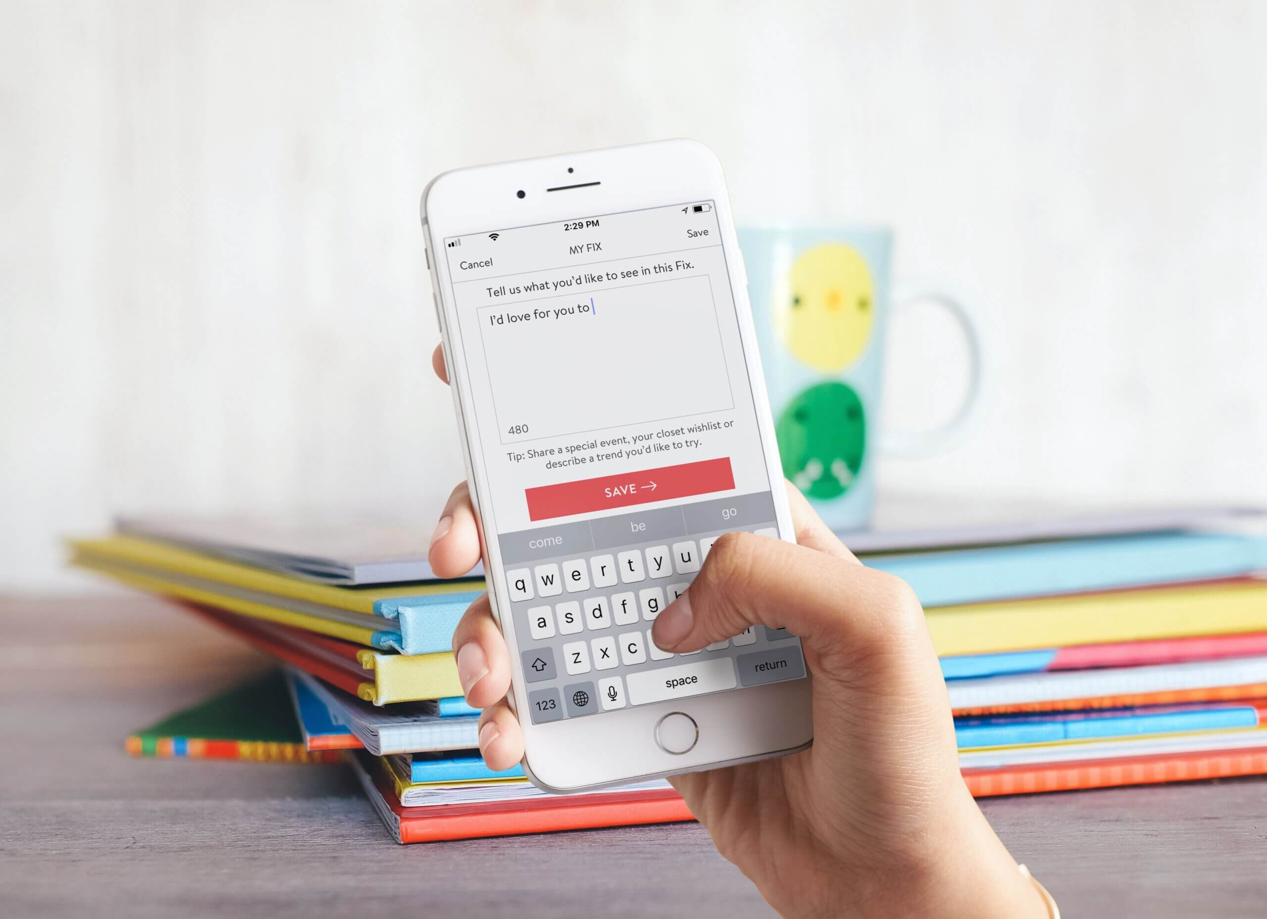 Stitch Fix mobile app displayed and demonstrated on iPhone with stacked books and mug on desk.