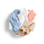 Stitch Fix Women’s outfit featuring coral jeans, blue embroidered blouse, white button-down, embroidered sandals and straw clutch.