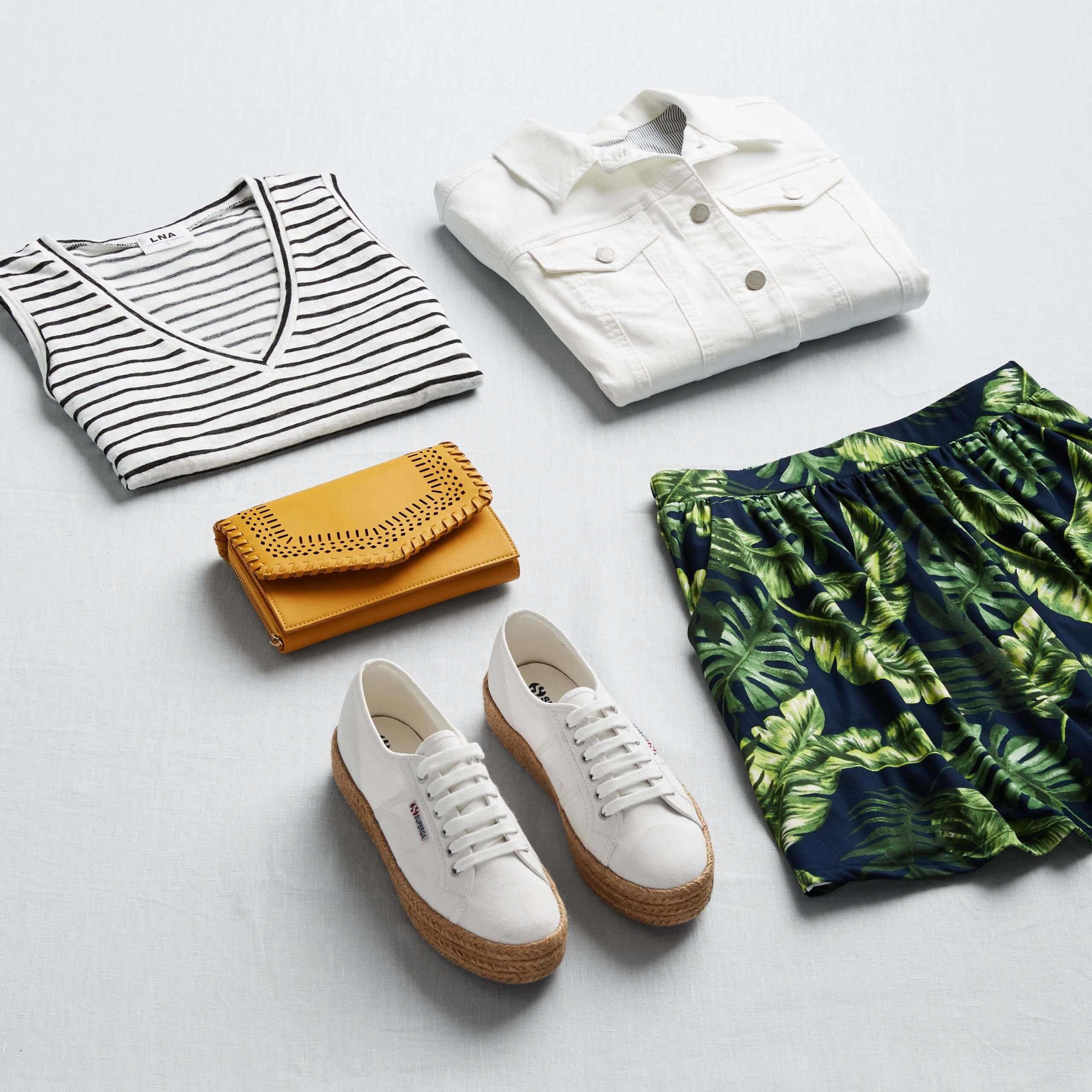 Stitch Fix women’s outfit showing how to mix prints and patterns featuring striped top, white denim jacket, yellow clutch, palm-print shorts and white sneakers.