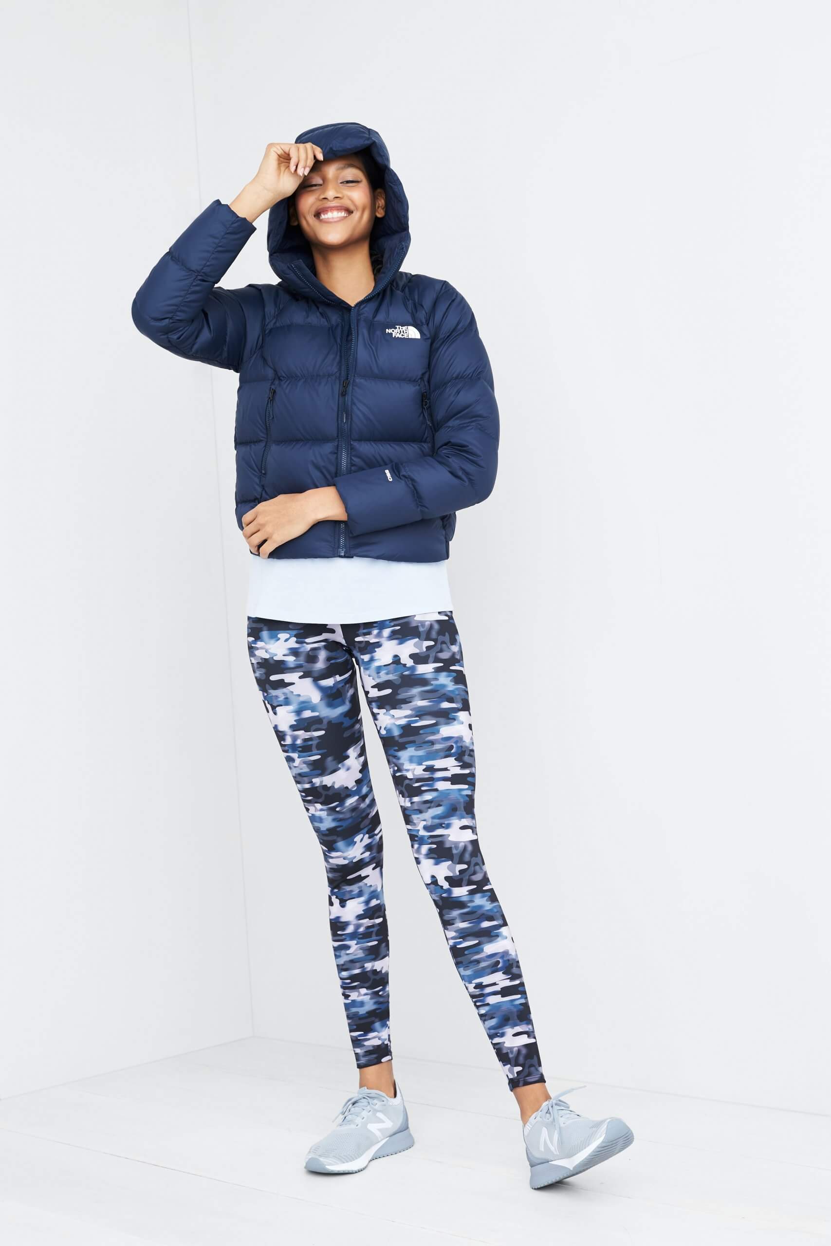 Stitch Fix model wearing eco-friendly clothing featuring blue patterned leggings, light blue tank, navy puffer jacket and grey sneakers.