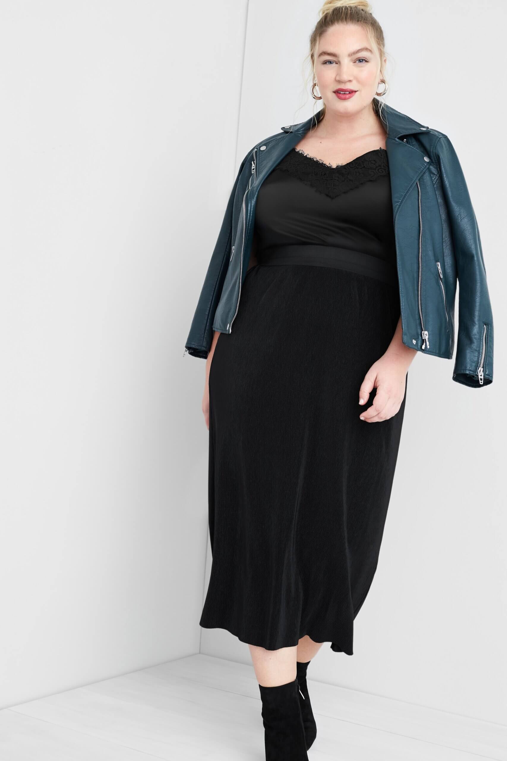 Stitch Fix women’s model wearing black lace bodysuit outfit with black ribbed midi skirt, teal green moto jacket and black booties.