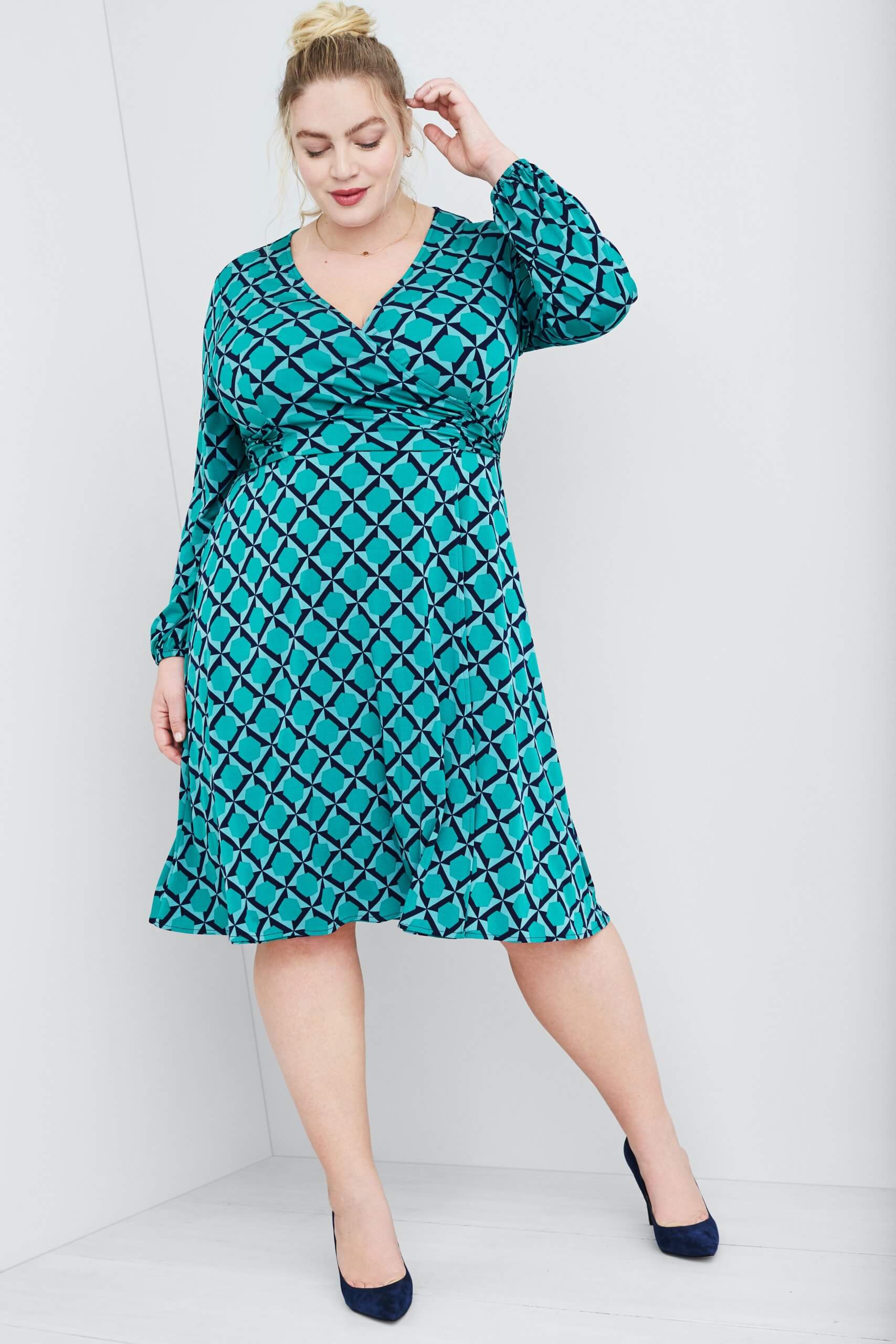 Stitch Fix Women's model wearing teal green abstract print wrap dress and navy heels.