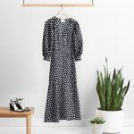 Stitch Fix women’s black and white polka-dot dress on hanger with black wedges on wooden table and two potted plants.