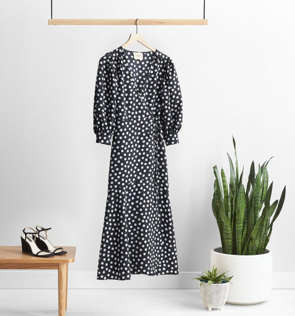 Stitch Fix women’s black and white polka-dot dress on hanger with black wedges on wooden table and two potted plants.