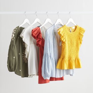 Stitch Fix women’s blouse assortment in olive green, white, orange, blue and white stripes and yellow tops with puff sleeves and flutter sleeves hanging on clothing rack.