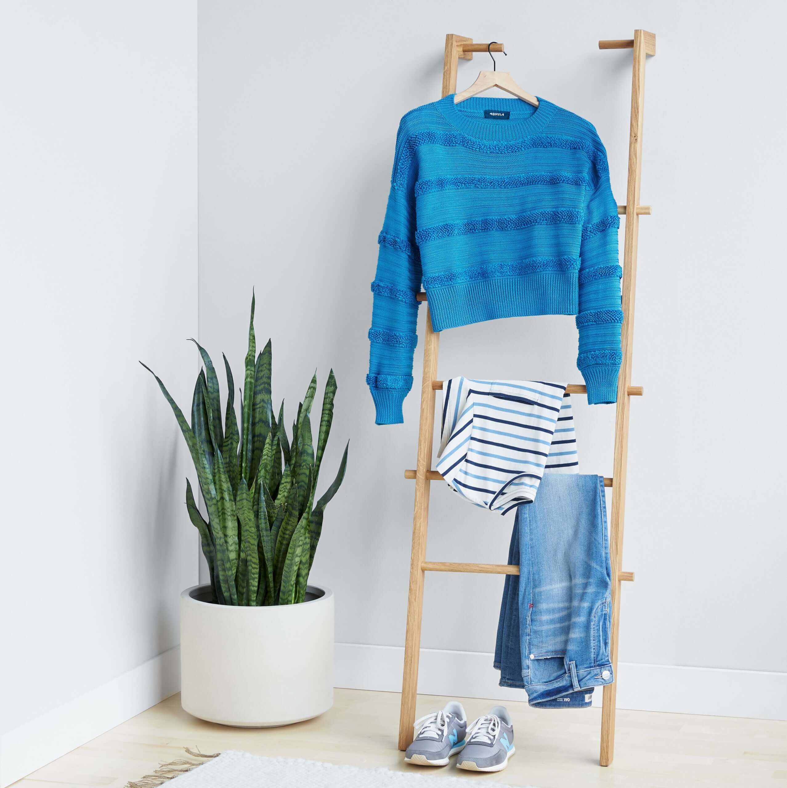 Stitch Fix women's outfit featuring blue textured pullover sweater, white and blue striped shirt and blue jeans hanging on wooden ladder, next to blue sneakers. 