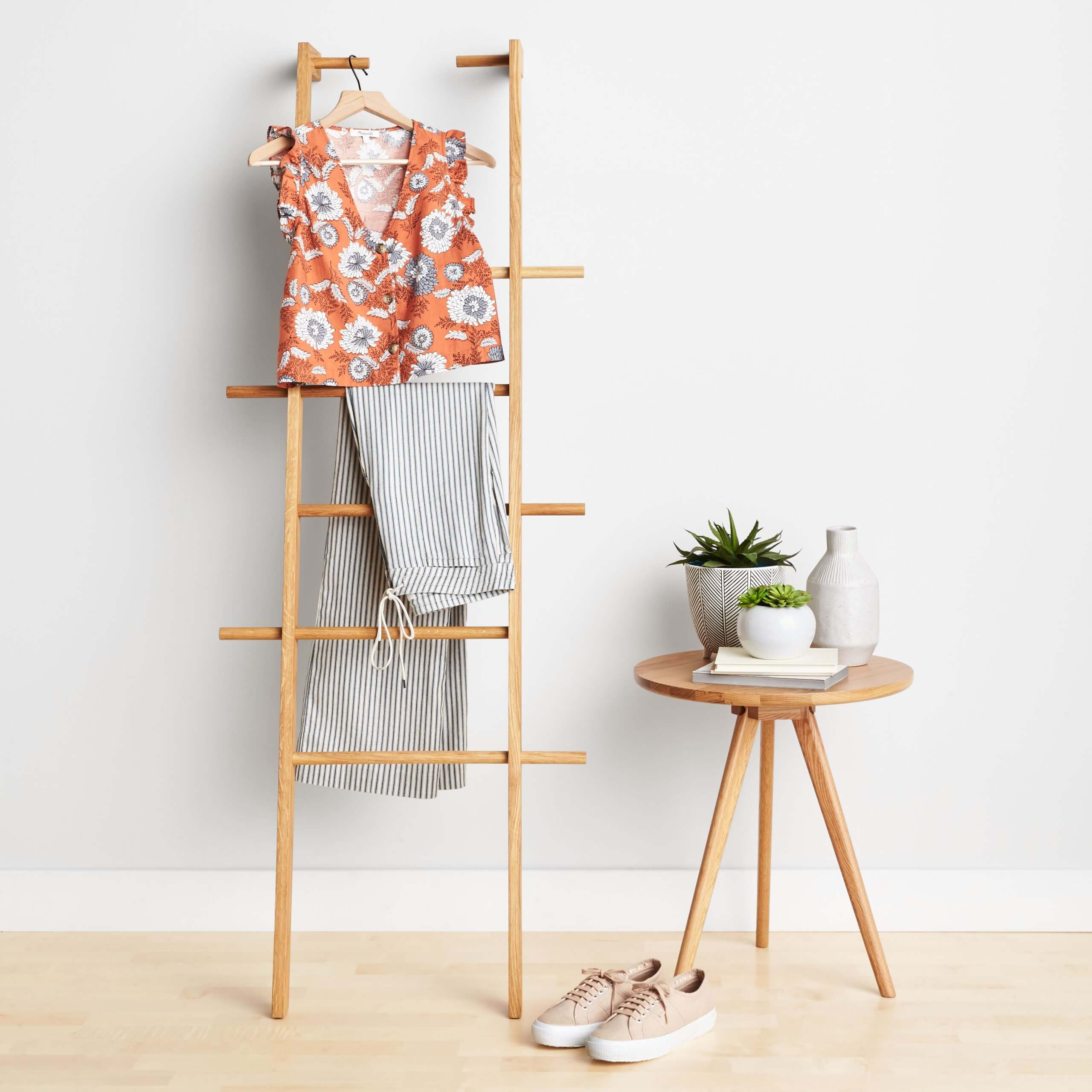 Stitch Fix women’s orange and blue floral blouse with striped pants hanging on ladder. Tan sneakers next to table with vases.