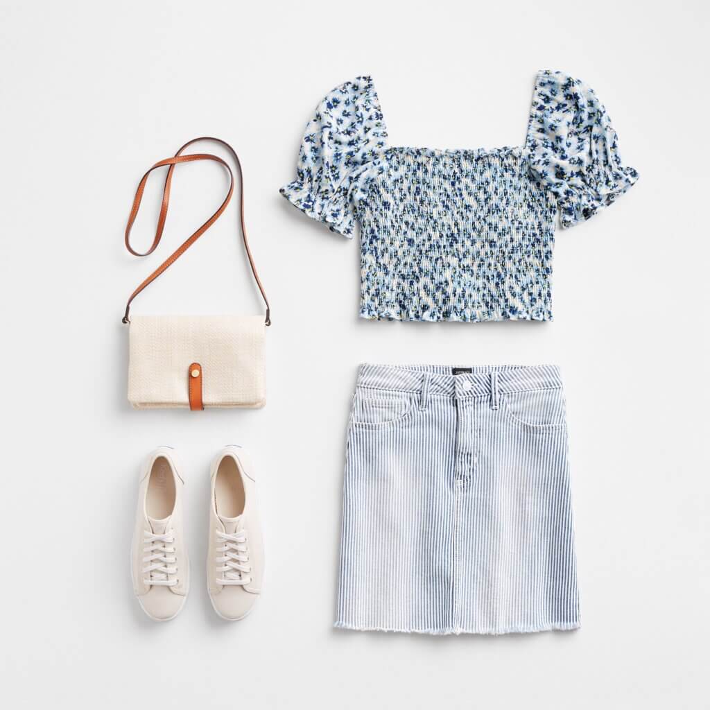 Stitch Fix Women’s Easter outfit featuring striped denim skirt, blue ditsy floral smocked top with puff sleeves, white sneakers and crossbody bag.