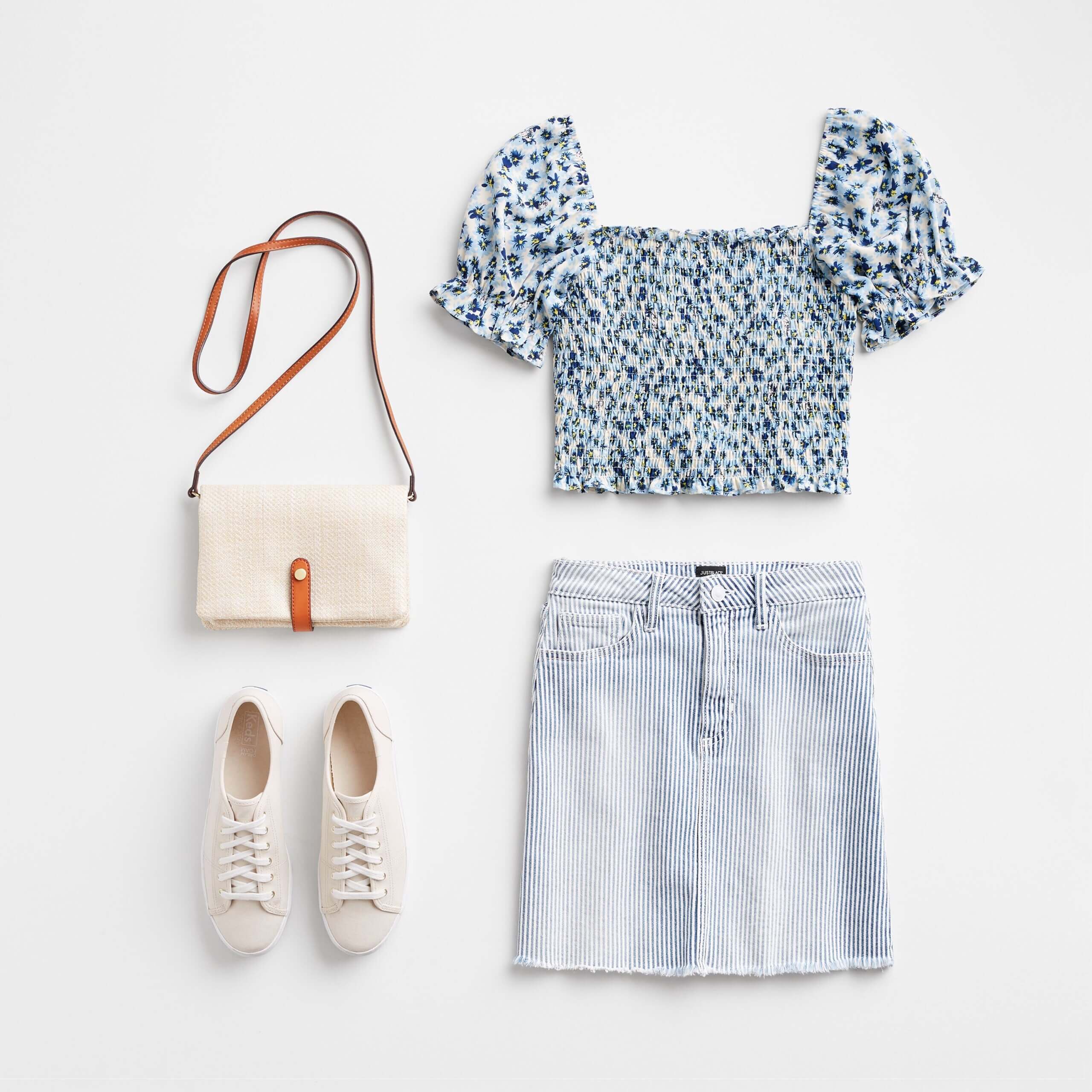 Stitch Fix Women’s Easter outfit featuring striped denim skirt, blue ditsy floral smocked top with puff sleeves, white sneakers and crossbody bag.