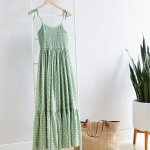 Stitch Fix Women’s green tiered maxi dress hanging on clothing rack next to a potted plant. Featured with straw tote and red wedge sandals.
