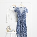 Stitch Fix Women’s rack image featuring white denim jacket and blue and white printed midi dress on hangers on white rack, next to blue wedges on a white stool.