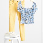 Stitch Fix women’s yellow skinny jeans and blue floral blouse hanging on rack. White sneakers on a white stool.