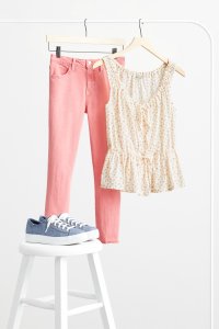 Stitch Fix women’s pink skinny jeans and yellow-patterned blouse hanging from a rack behind blue sneakers on stool.