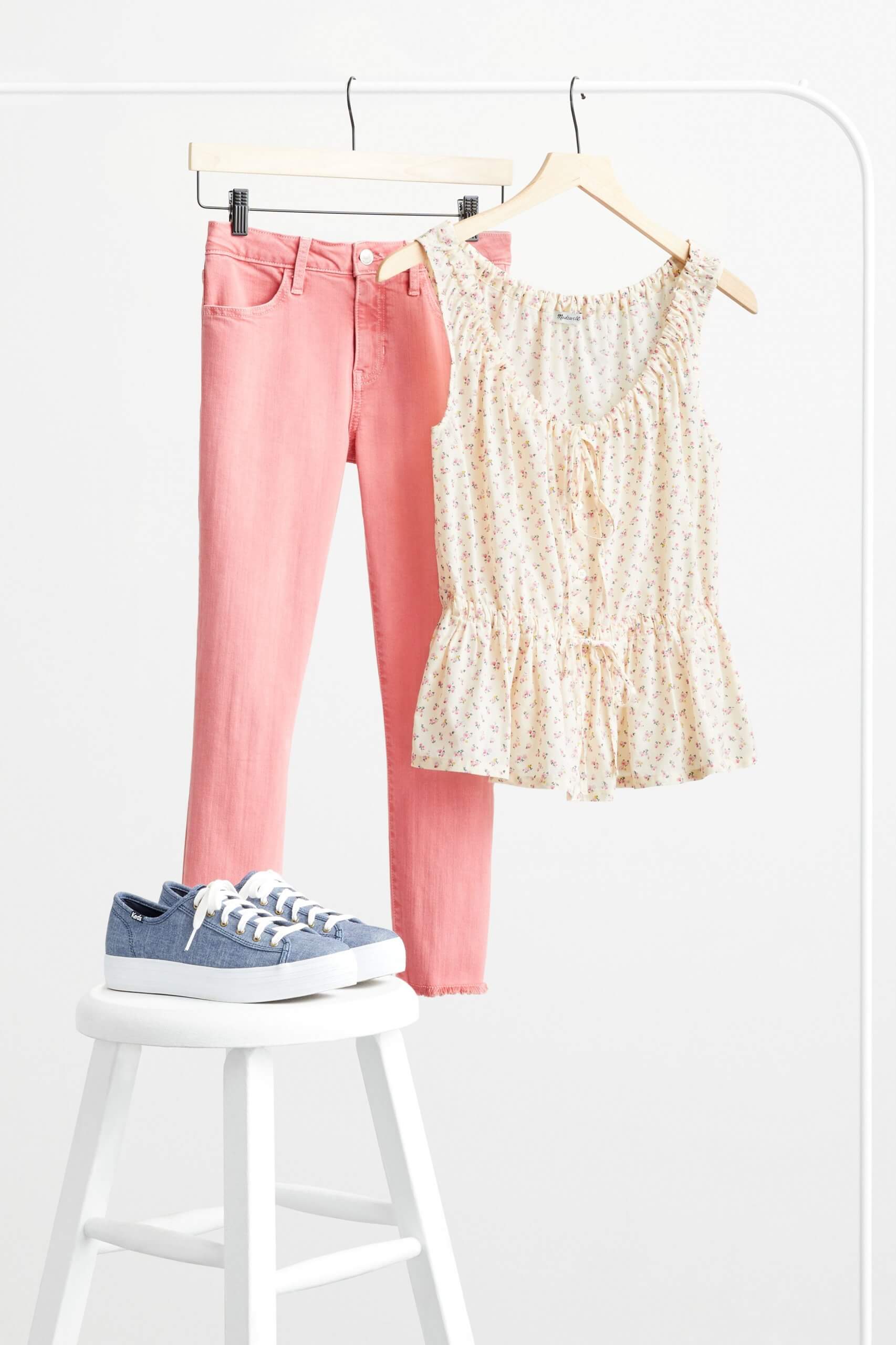 Stitch Fix Women’s pink skinny jeans and yellow-patterned blouse hanging from a rack behind blue sneakers on stool.