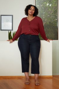 Stitch Fix model wearing red henley top with jeans and leopard-print flats standing in front of window, plant and picture.