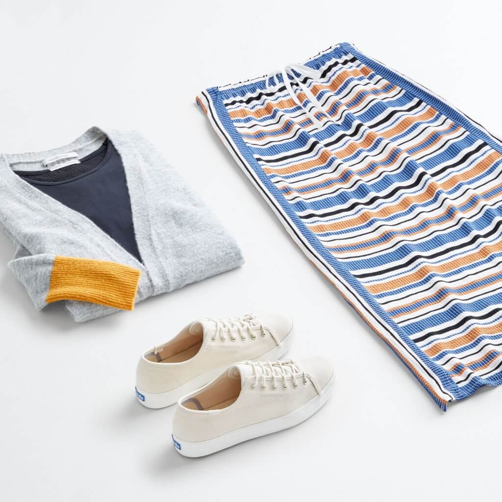Stitch Fix women’s outfit laydown featuring off-white sneakers, navy shirt under grey and yellow cardigan sweater and striped maxi skirt.