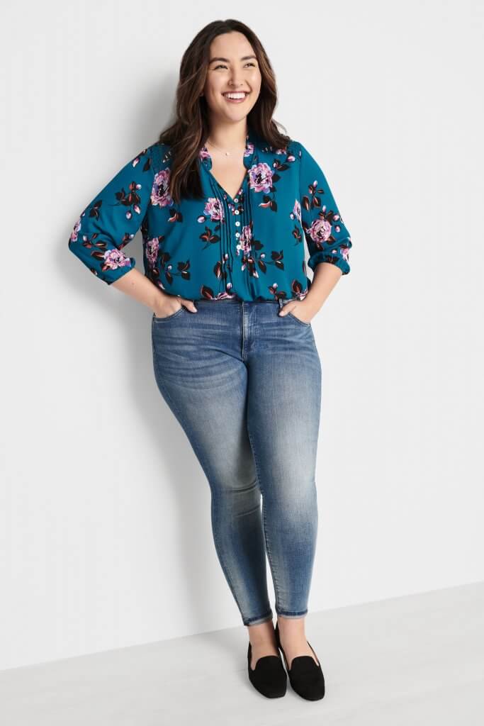 Stitch Fix model wearing a pendant necklace, a teal-blue floral blouse, faded medium-wash skinny jeans and black loafers.