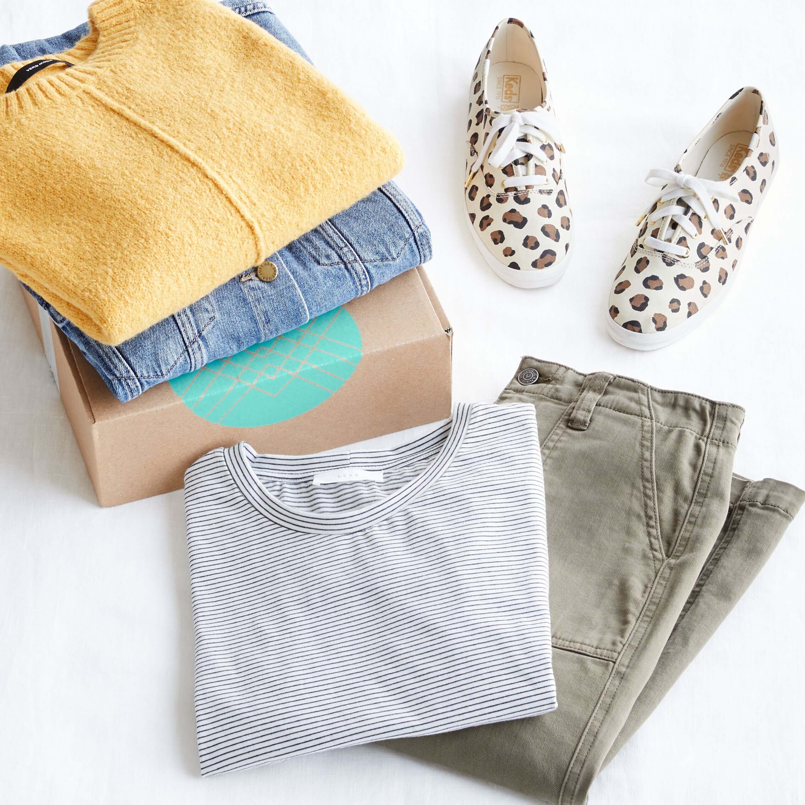 Stitch Fix cardboard box with denim jacket, yellow sweater, olive green cargo pants, black and white striped top and leopard print lace-up sneakers.
