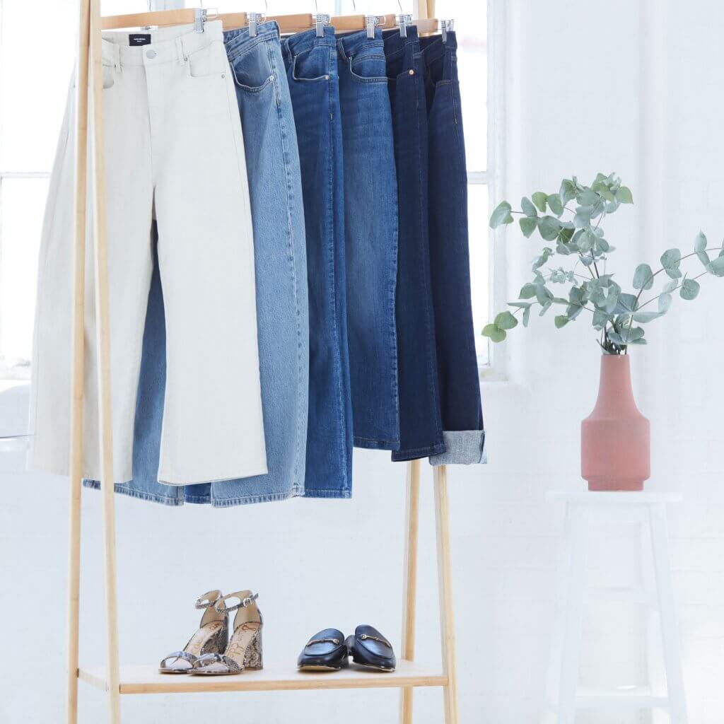 Stitch Fix Women’s rack with white, light blue, classic blue, and dark blue jeans hanging with shoes under, next to a plant.