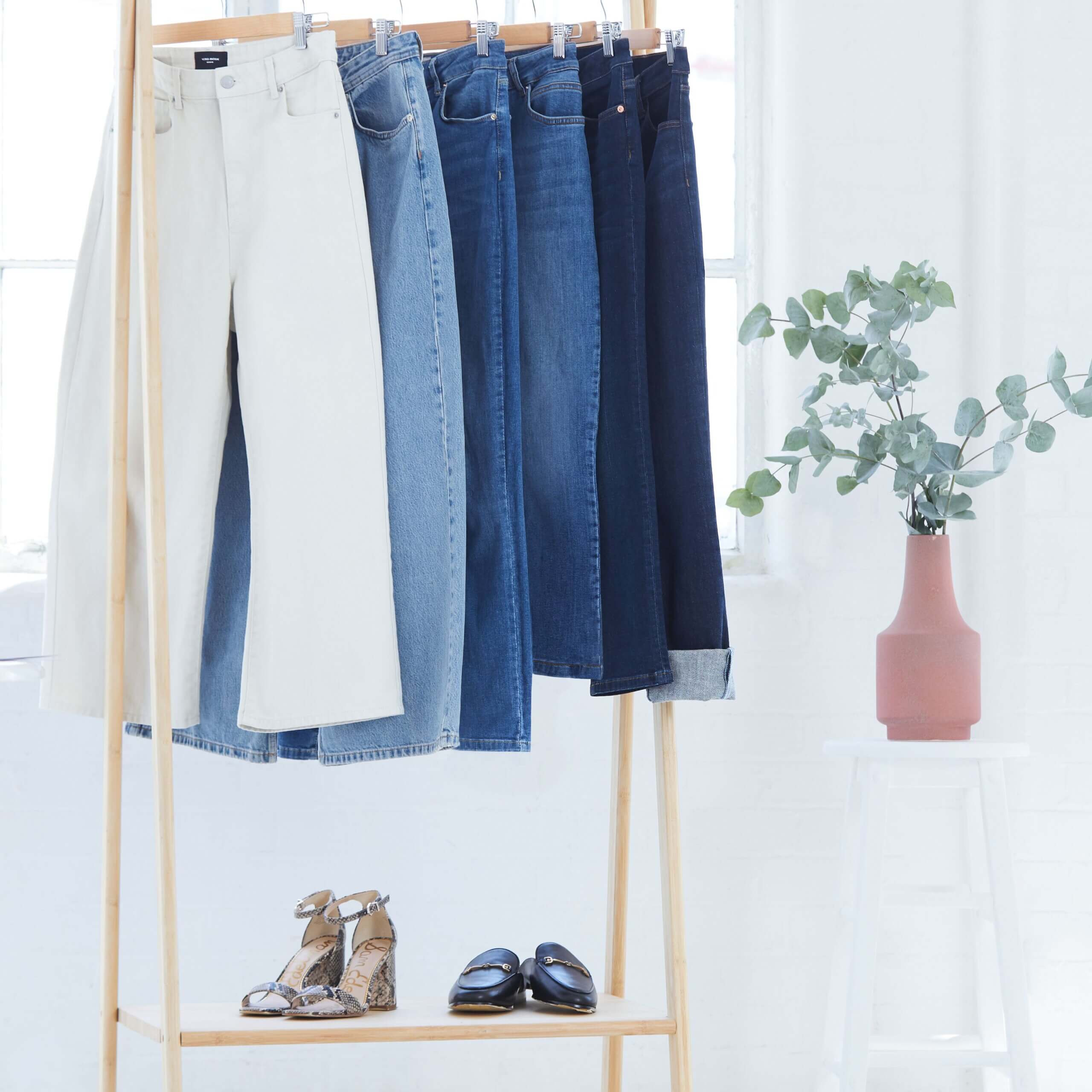 Stitch Fix Women’s rack with white, light blue, classic blue, and dark blue jeans hanging with shoes under, next to a plant.