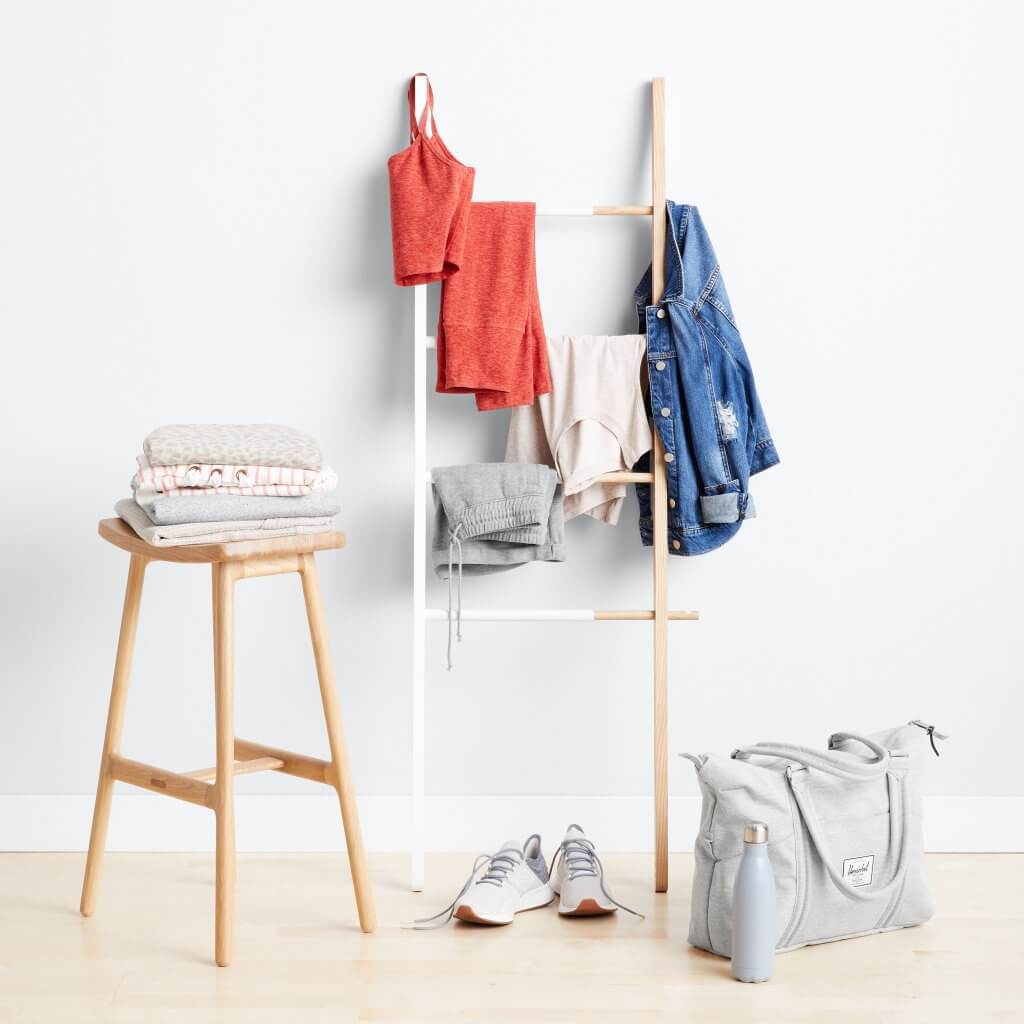 Stitch Fix women’s clothing four sweaters on a stool, red athletic wear, loungewear, denim jacket, grey sneakers and grey duffle bag.